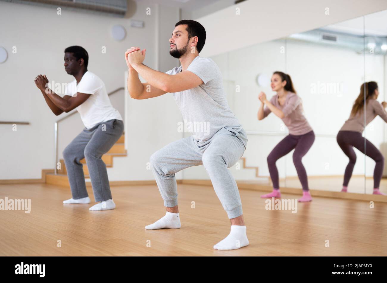 Young man doing squats during warm up before group yoga class Stock Photo