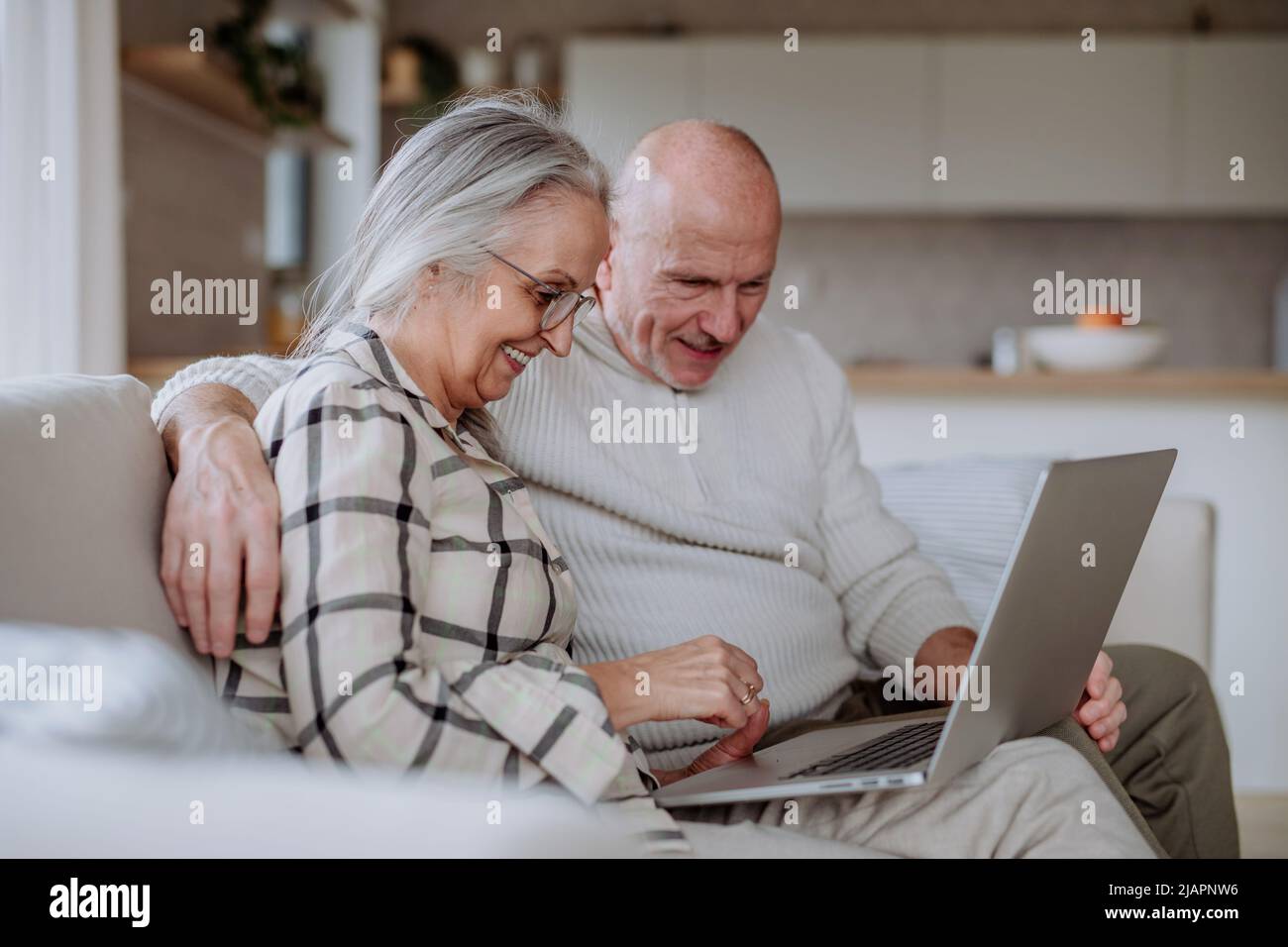 Senior couple sitting on sofa and using laptop together. Stock Photo