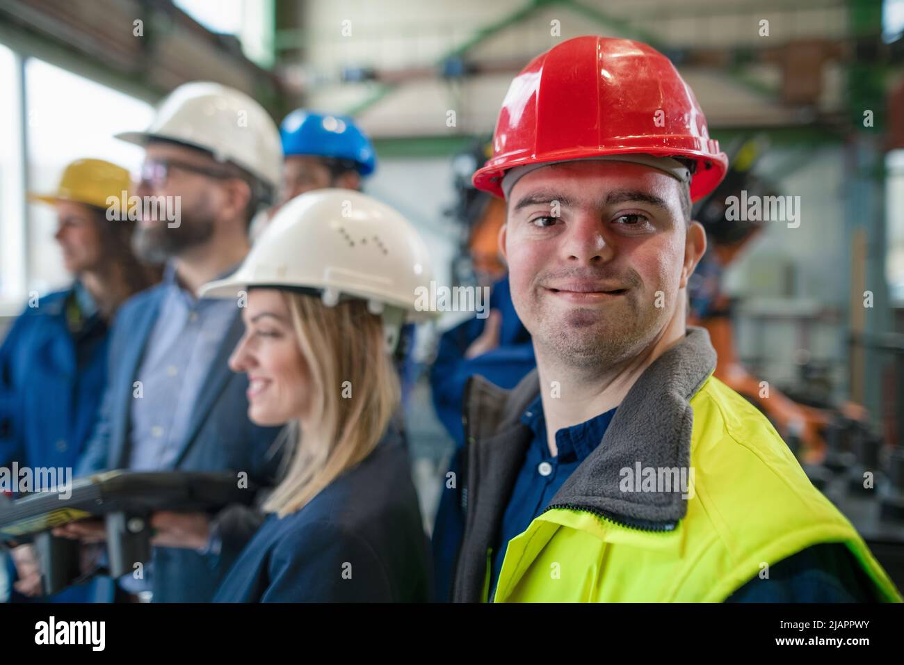 Young man worker with Down syndrome with manager and other collegues working in industrial factory, social integration concept. Stock Photo