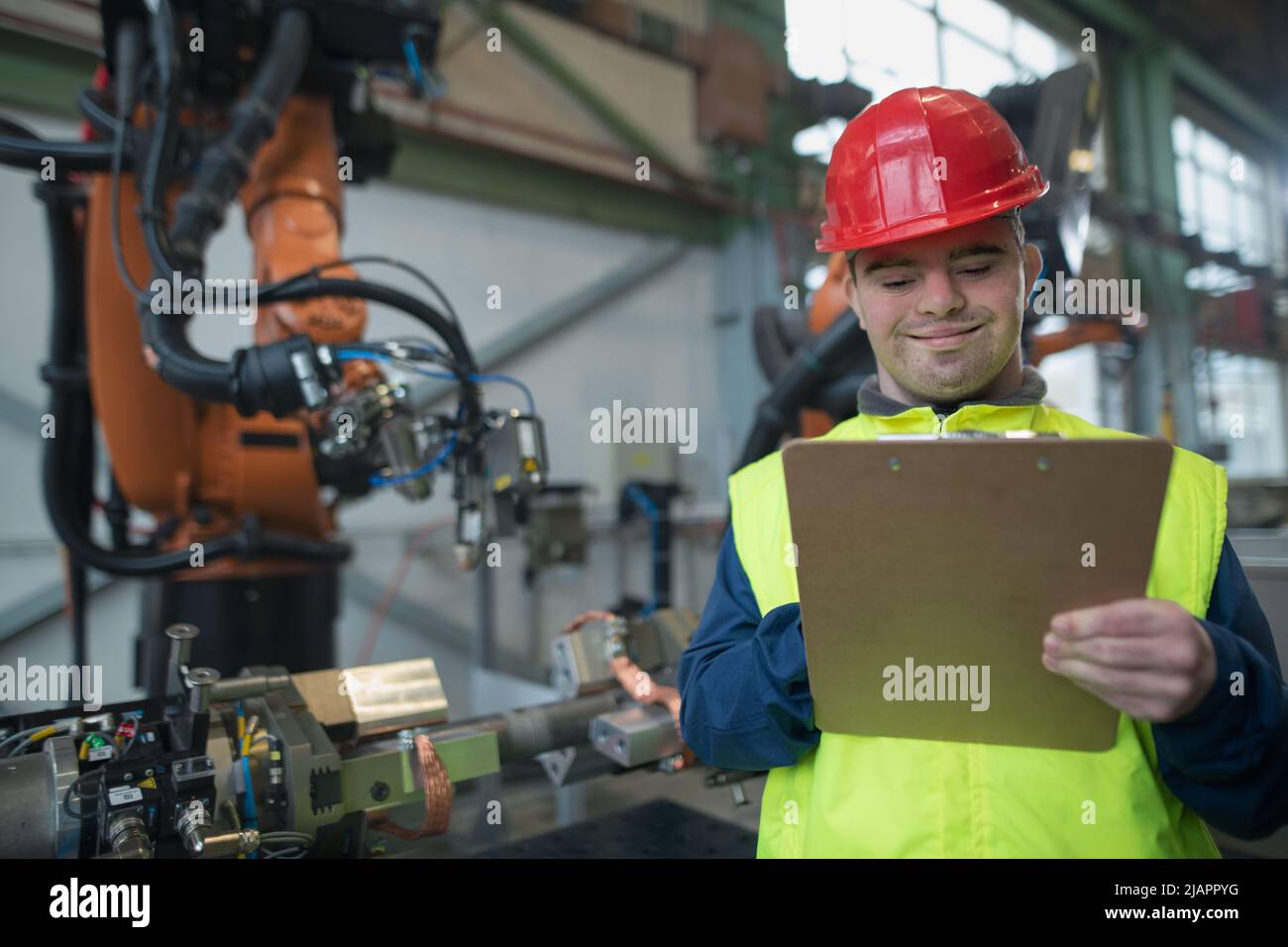 Young man with Down syndrome working in industrial factory, social integration concept. Stock Photo