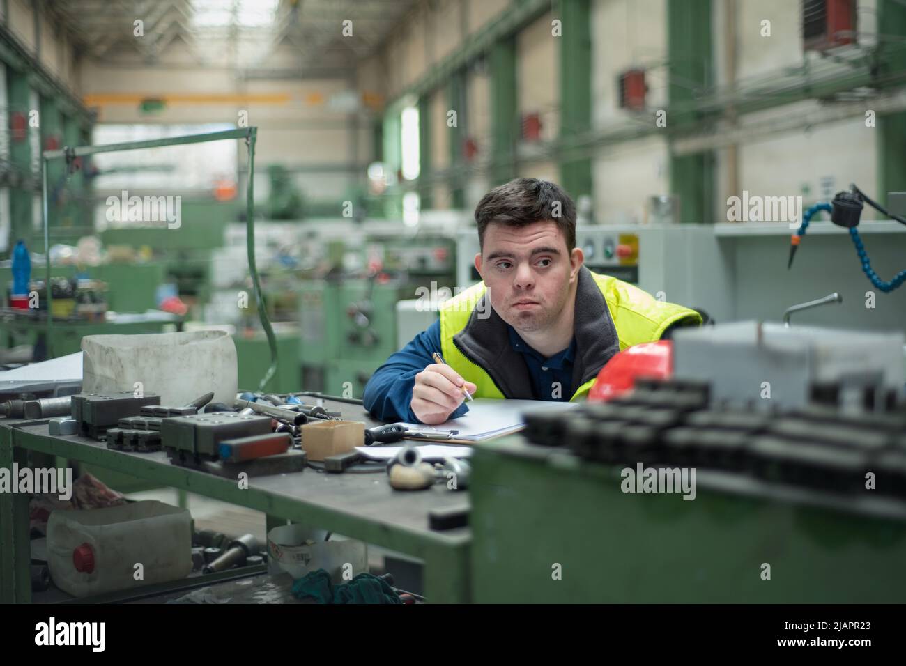 Young man with Down syndrome working in industrial factory, social integration concept. Stock Photo