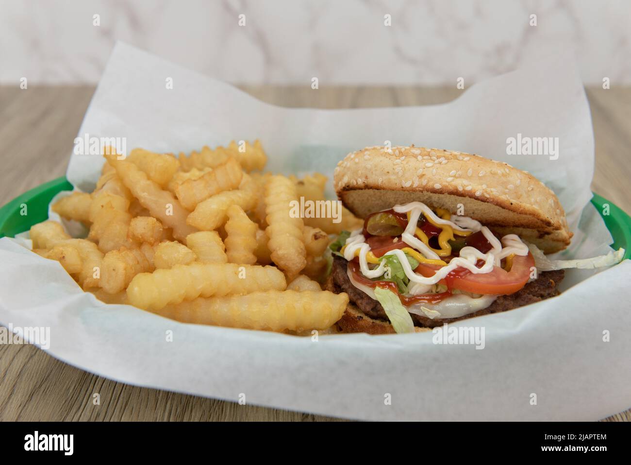 Loaded hamburger and crinkled french fries  served in a fast food basket. Stock Photo