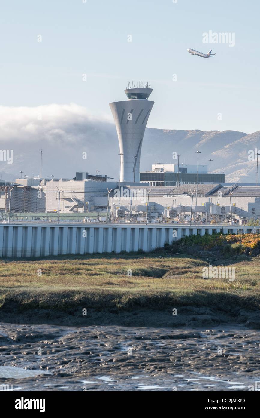 The airport traffic control tower at San Francisco international airport (SFO) in the Bay area of California with a plane taking off in the background. Stock Photo