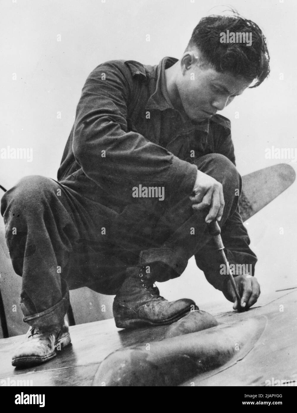 Original caption: During the campaign in Malaya, preparations were being made behind the lines to prevent equipment from falling into the hands of the advancing Japanese troops. At a Netherlands fighter squadron, a Javanese member of the ground staff closes one of the gun-bay panels on a Dutch Brewster Buffalo fighter ca.  January 1942 Stock Photo