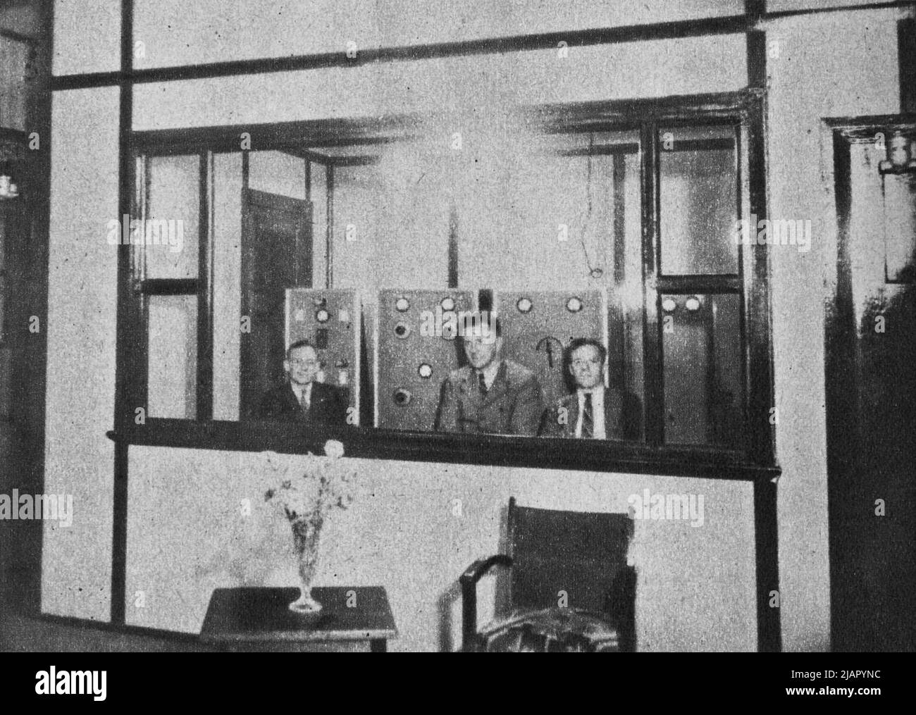 The transmitter. Through the studio window the engineers from left to right are Mr. P. R. Roberts, A.I.R.E., chief, who built and installed the plant. Mr. Trevor Evans, A.I.R.E., and Mr. J. E. Jarvis, B.O.C.P., engineer in charge of the 2BS plant. ca.  1937 Stock Photo