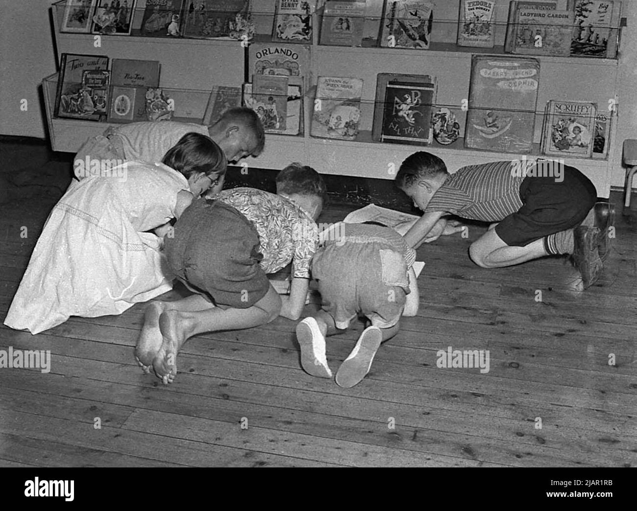 Children in a library sitting on the floor looking at books ca. 1955 Stock Photo