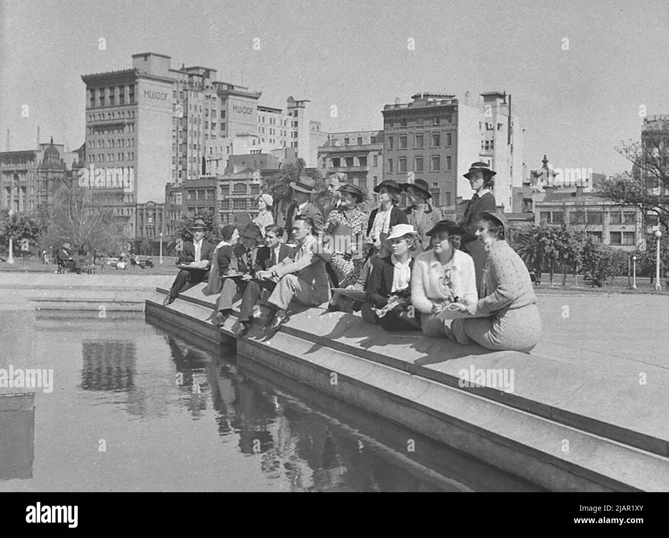 Group of men and women sitting near a pond in a city, possibly Sydney Australia ca. 1936 Stock Photo