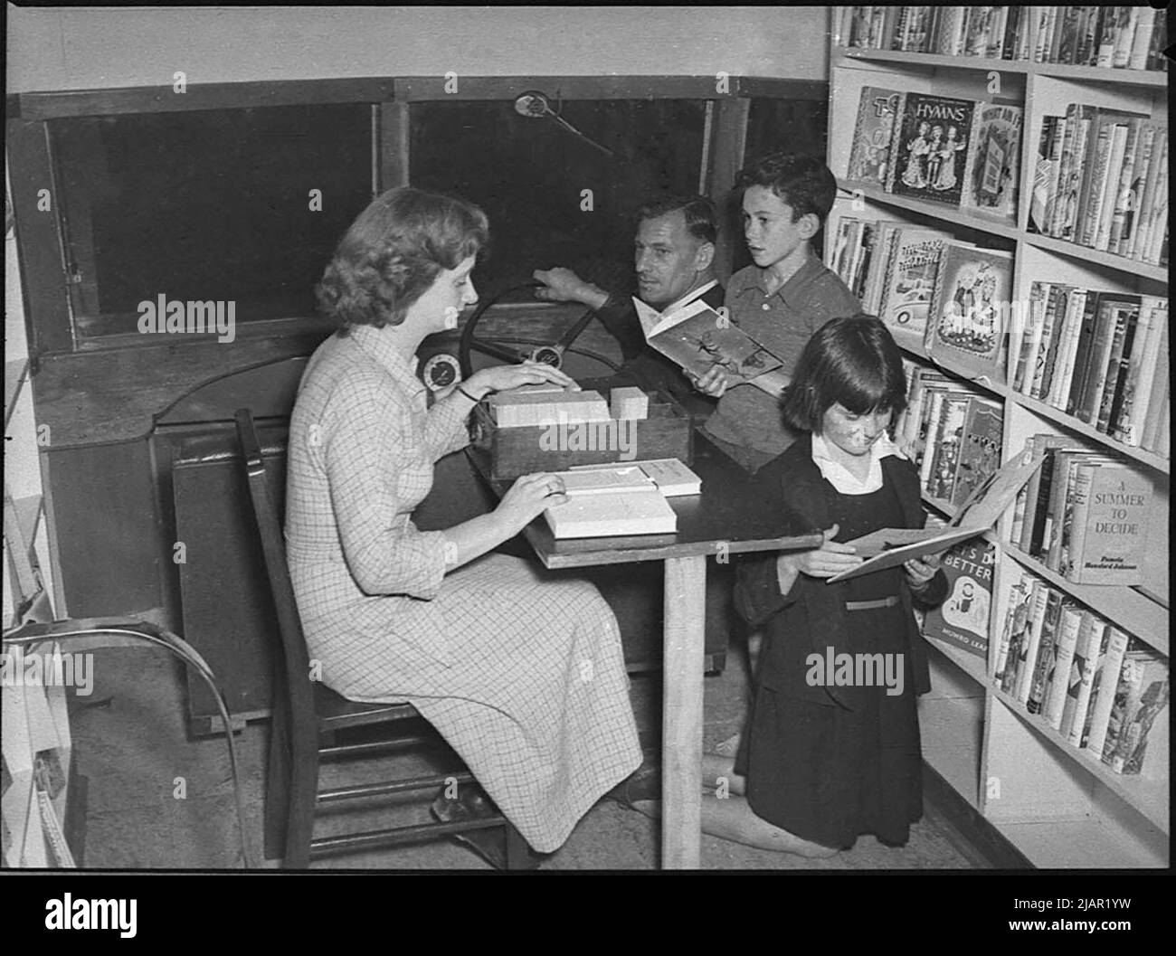 A family looking at books in a mobile library  or bookmobile in Australia ca. 1950 Stock Photo