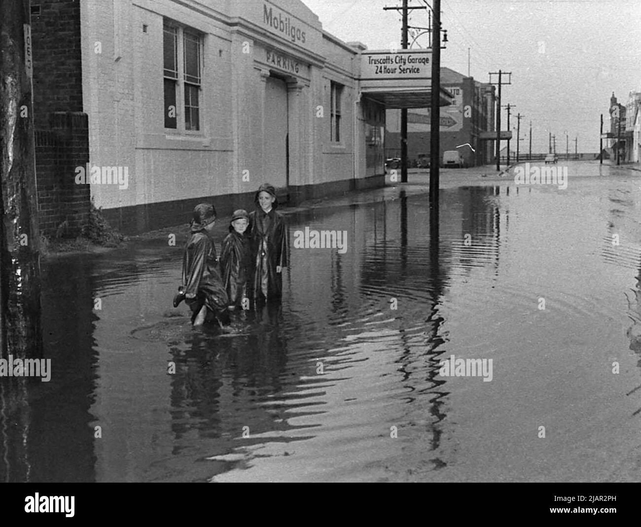 Children walking in flooded streets in front of a Mobilgas station in Australia ca. 1956 Stock Photo