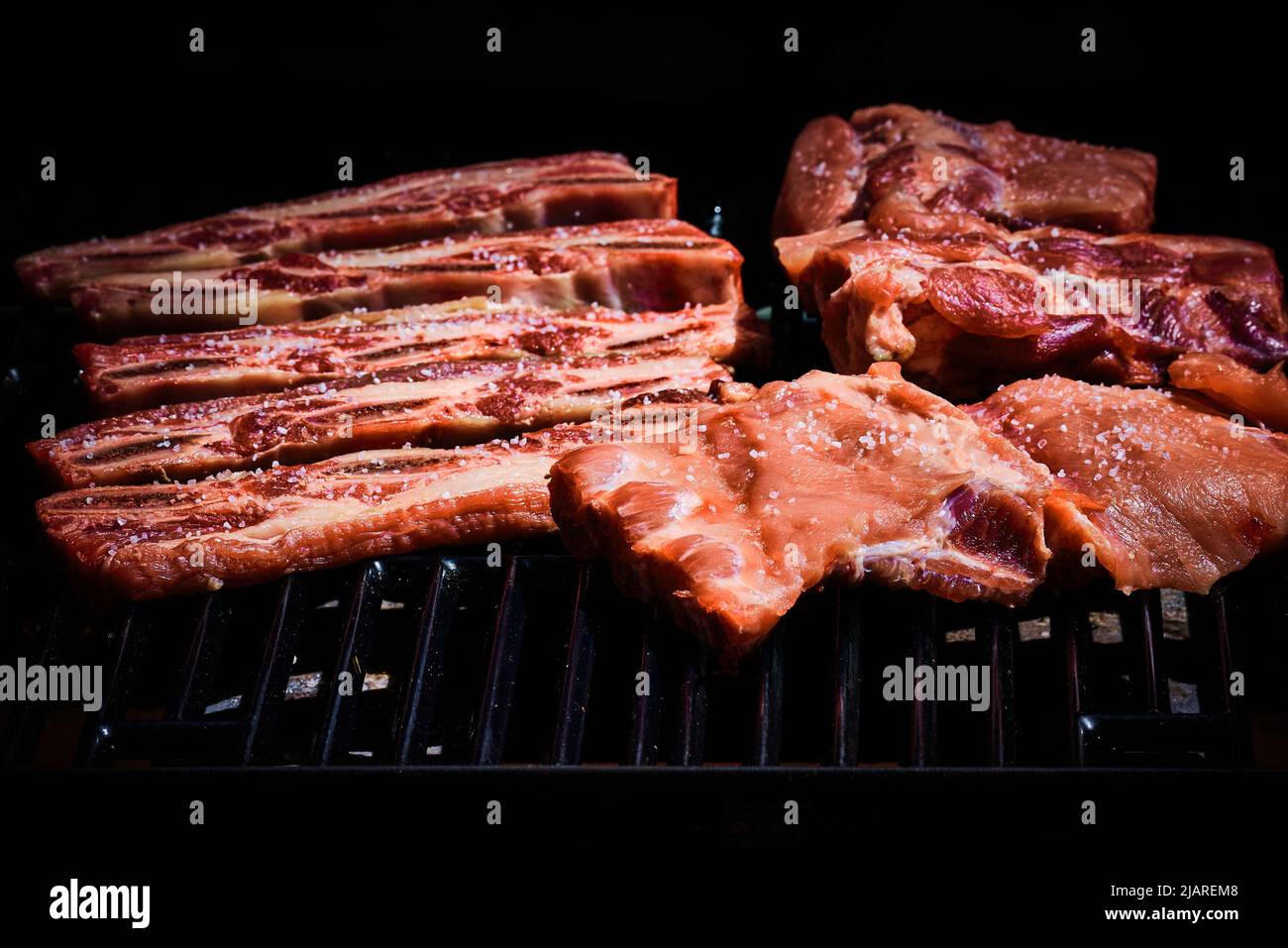Beef rib and pork rib freshly put on the barbecue to start grilling Stock Photo