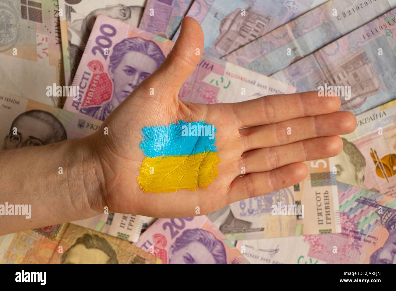 The yellow-blue flag of Ukraine is painted on the girl's hand on the background of money. Martial law in Ukraine 2022. Stop the war. Finance Stock Photo