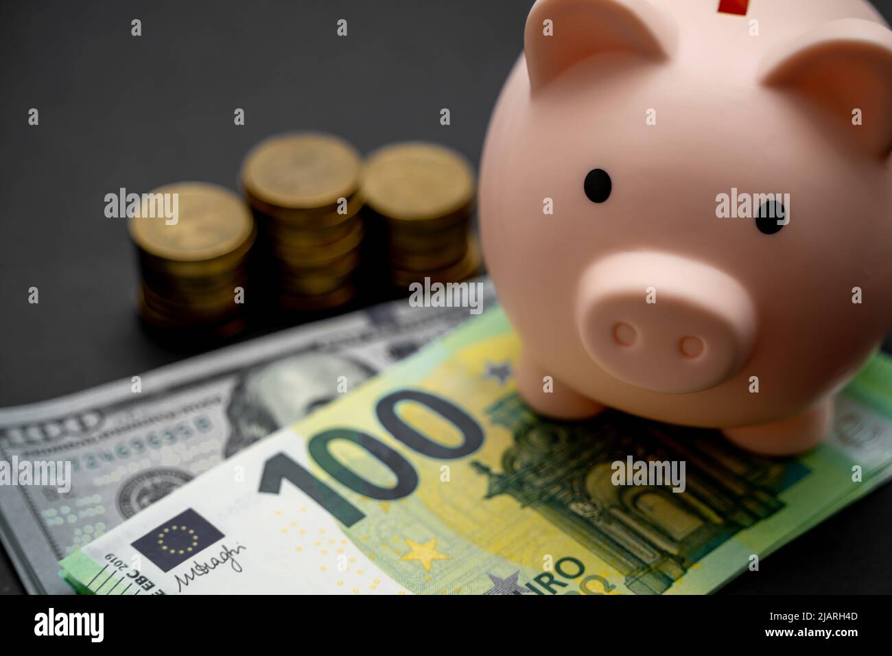 Pink piggy bank and a stack of dollars, euros and coins on a black ...