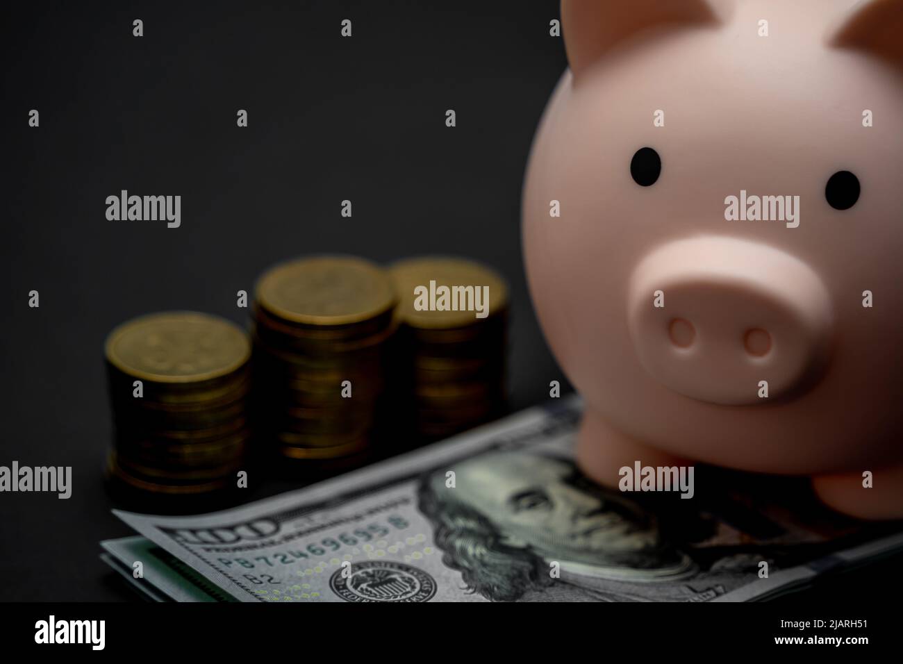 Pink piggy bank and a stack of dollars and coins on a black background ...