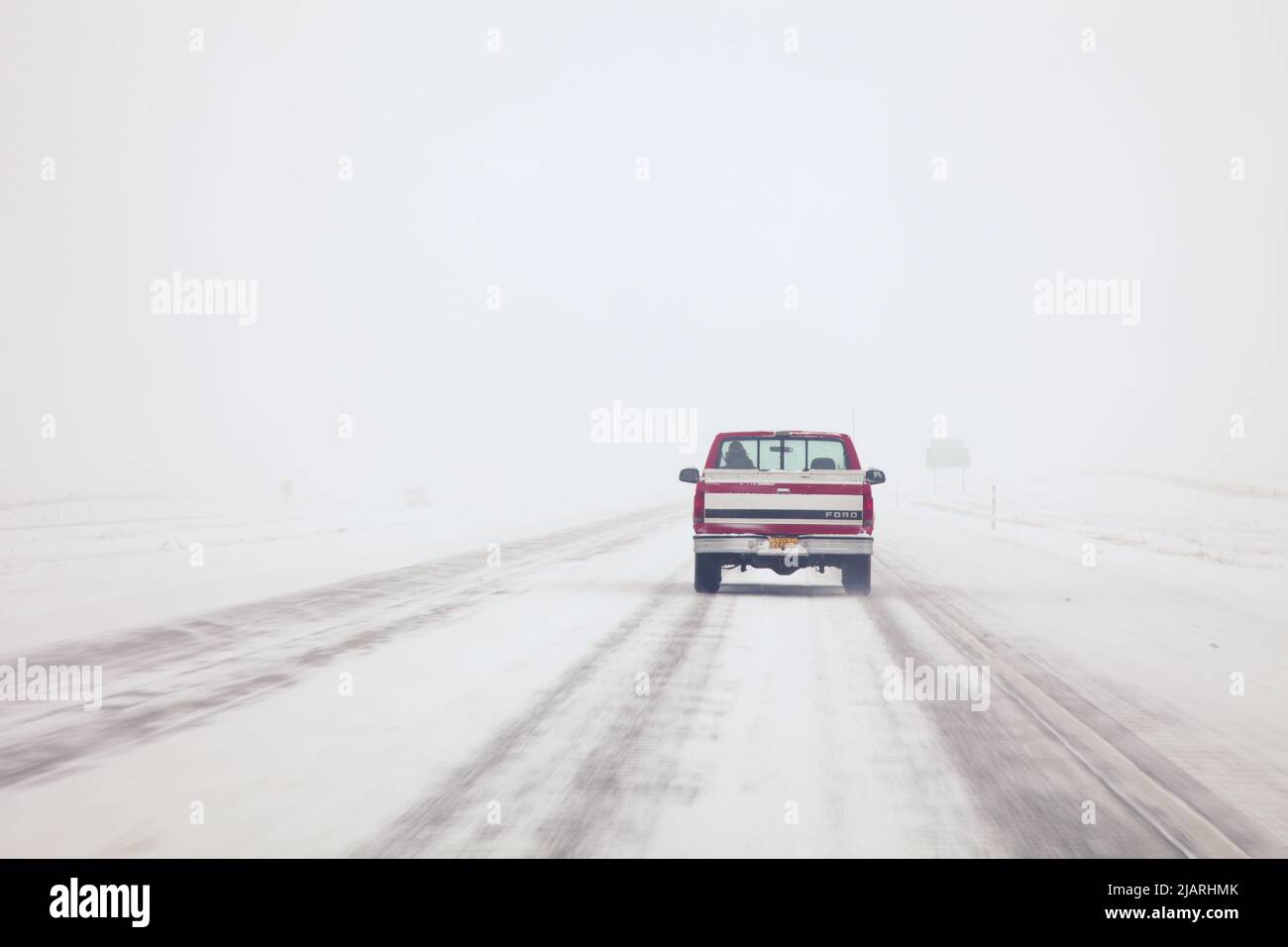 A red Ford pick up truck driving into white out snowy conditions in Oregon in December Stock Photo
