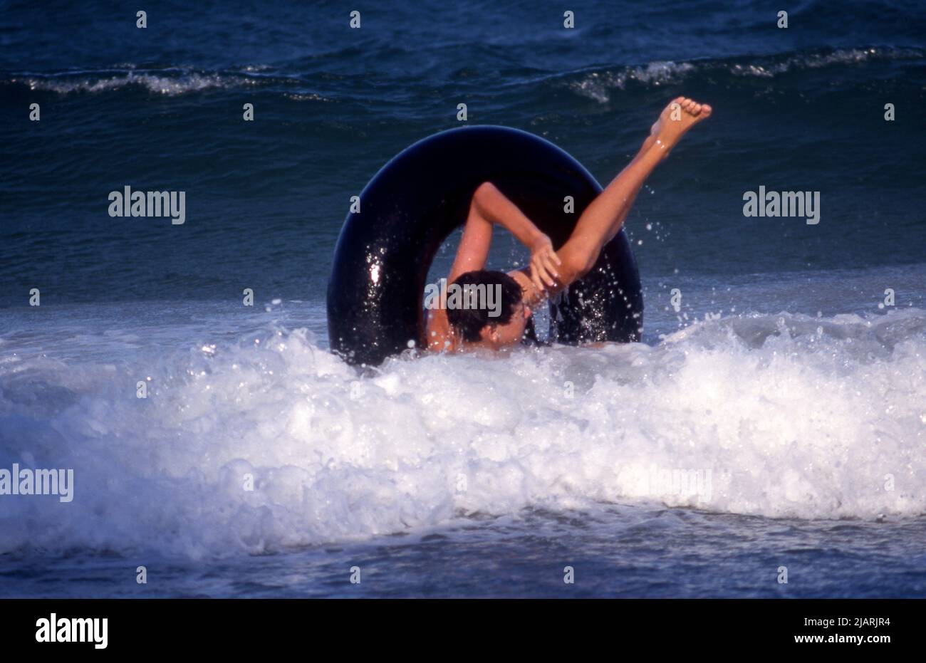YOUNG LAD IN THE OCEAN HAVING FUN IN HIS TYRE TUBE RUBBER RING. AUSTRALIA. Stock Photo