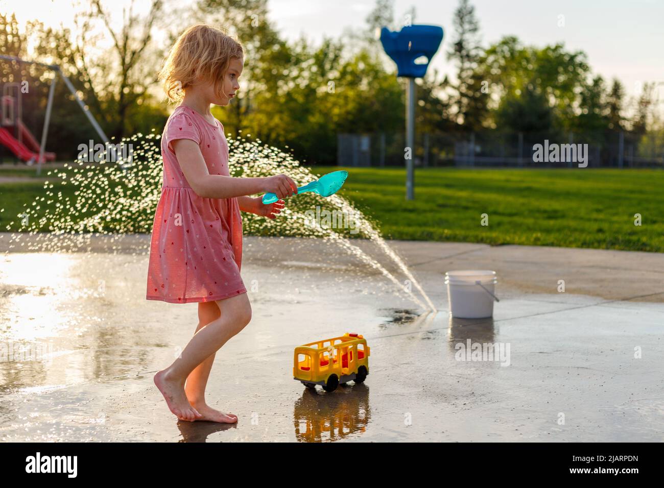 Small child playing with outdoor toys at splash pad playground in summer. Water park with fountains for children. Summertime activities for kids Stock Photo
