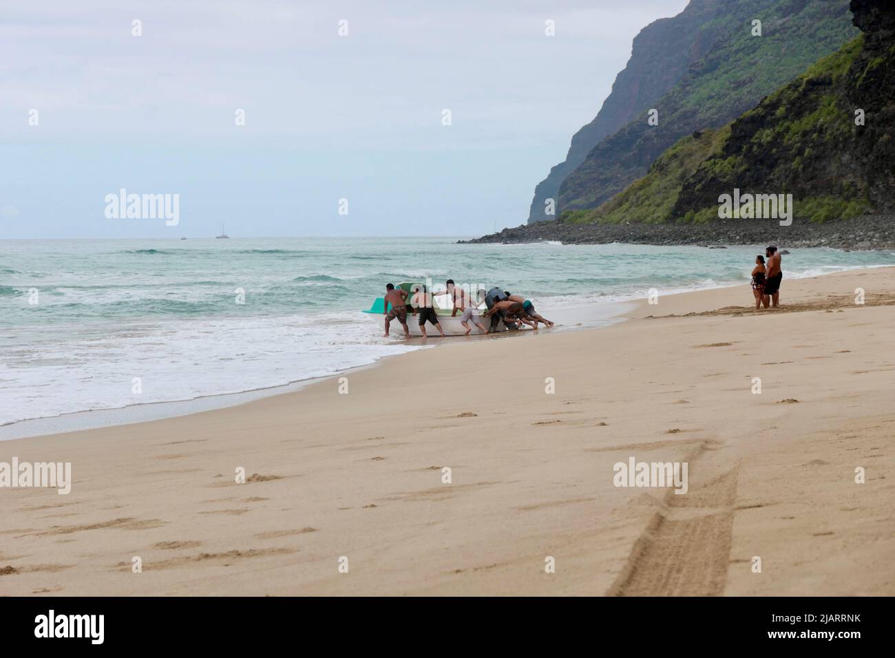 Family pushing boat into the water at Polihale Beach on Kauai Stock Photo