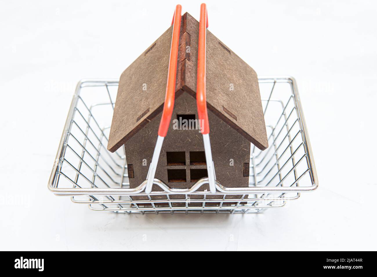 Toy wooden house in a shopping cart on a neutral background. Stock Photo