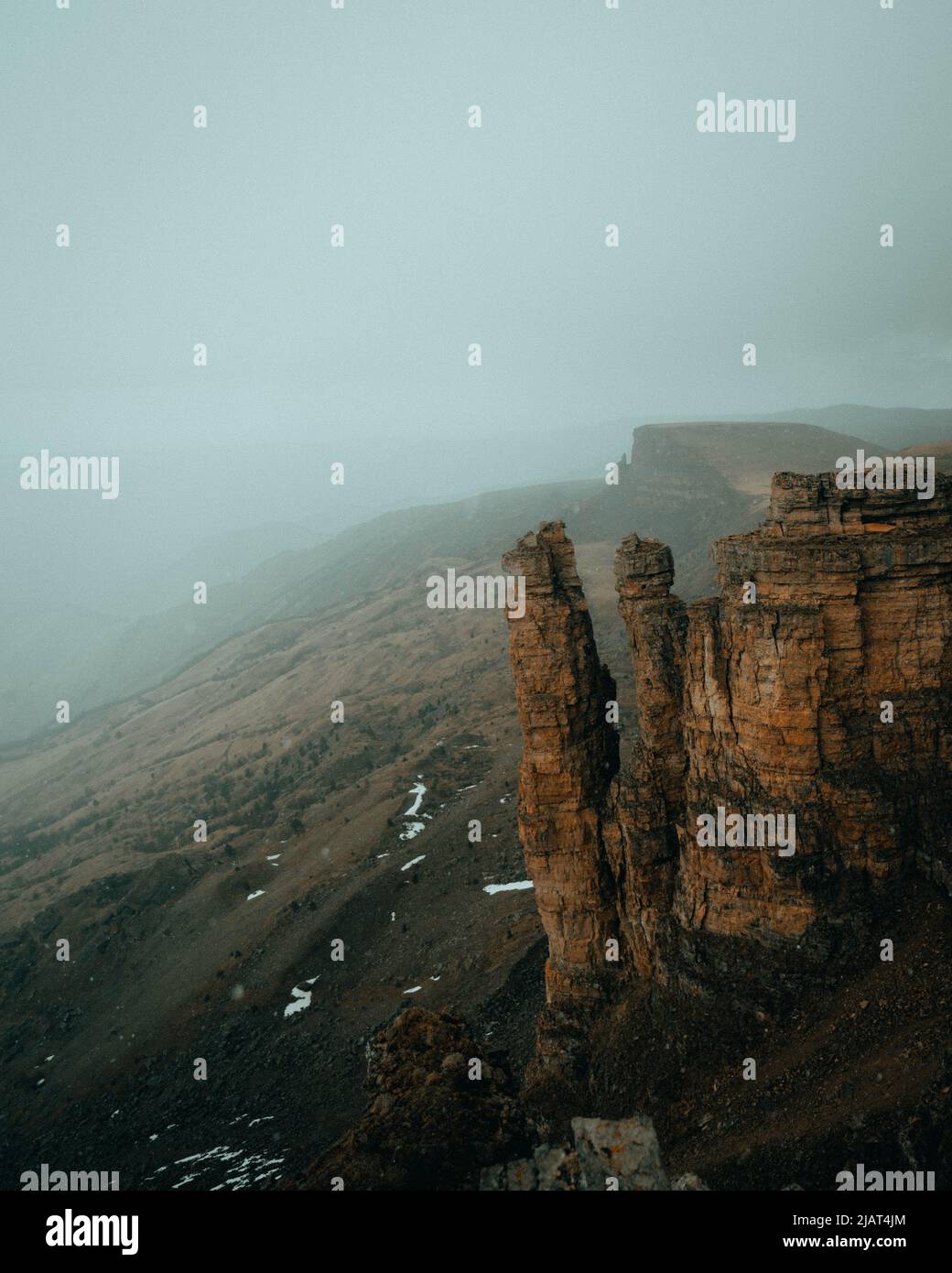 sheer cliffs in a foggy haze from the height of a neighboring peak Stock Photo