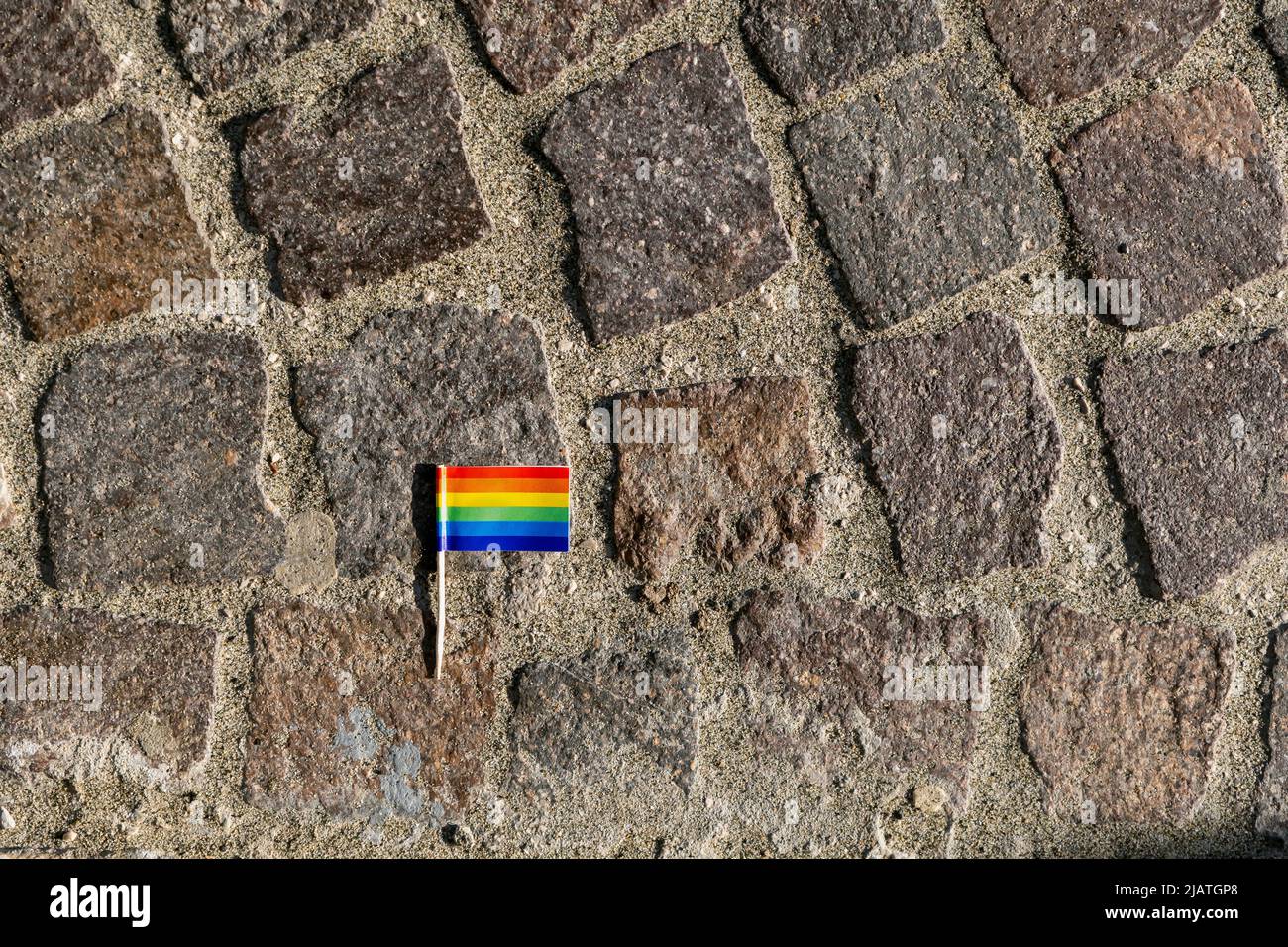 Toothpick rainbow flag on cobblestone pavement. Gay pride symbol. Copy space. Stock Photo