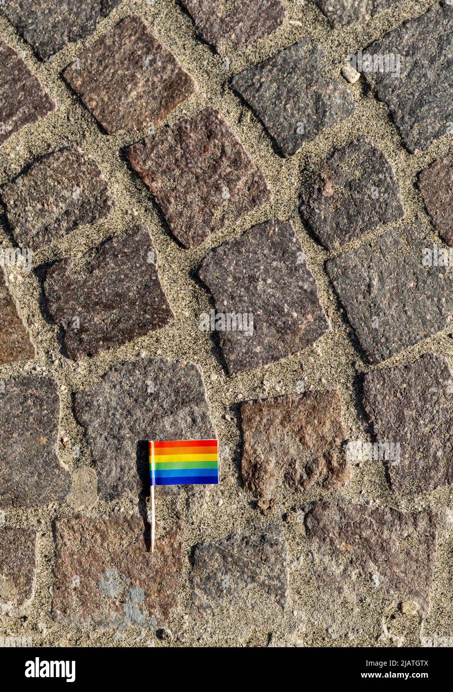 Toothpick rainbow flag on cobblestone pavement. Gay pride symbol. Copy space. Stock Photo