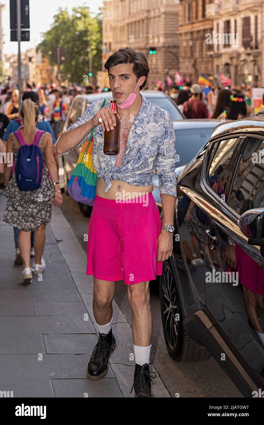 Young man dressed as a woman in a pink skirt, drinking a beer while walking down the street during gay pride. Rome, Italy, Europe, European Union, EU Stock Photo