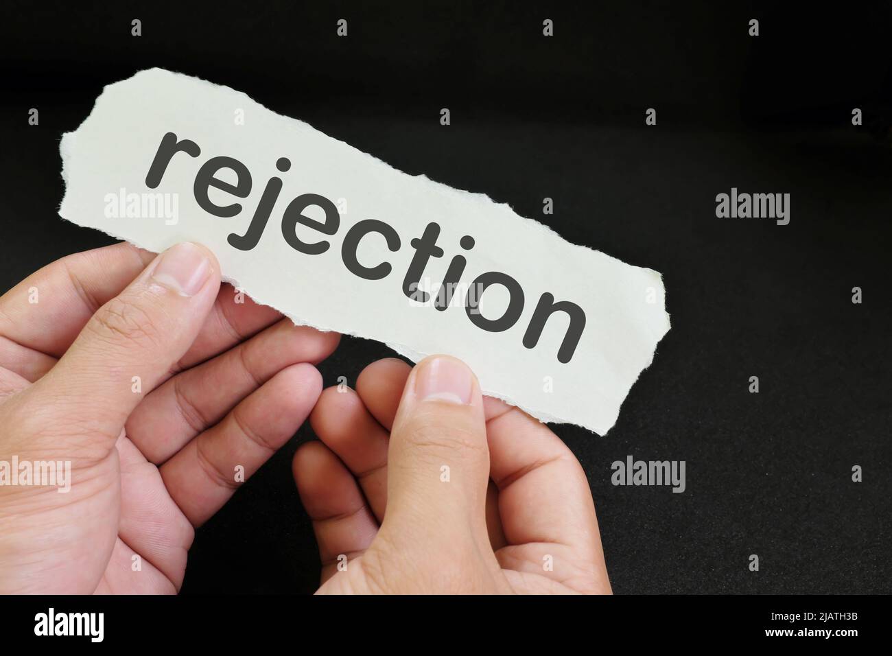 Hand holding a paper with written word rejection in black background