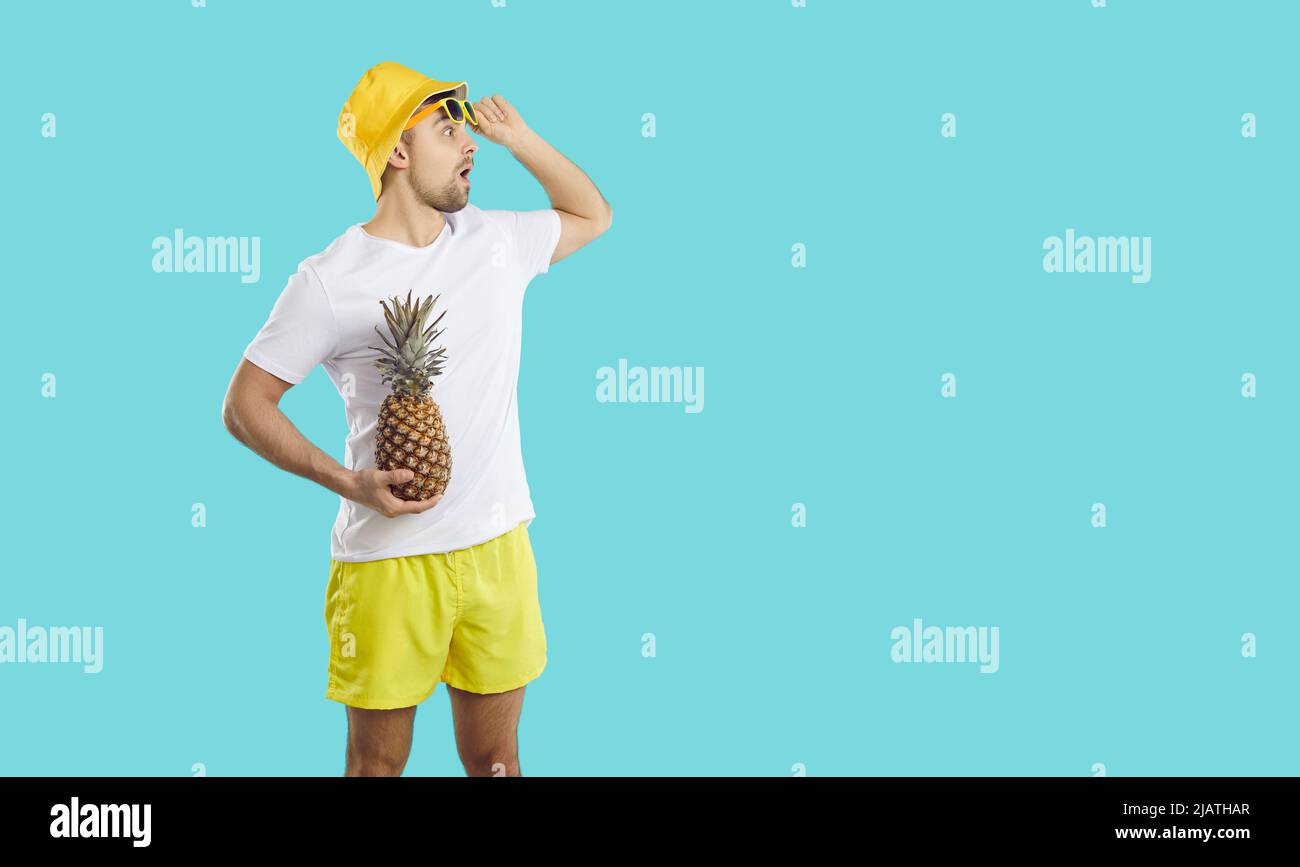 Man in summer clothes holding pineapple and looking at copy space with surprised expression Stock Photo