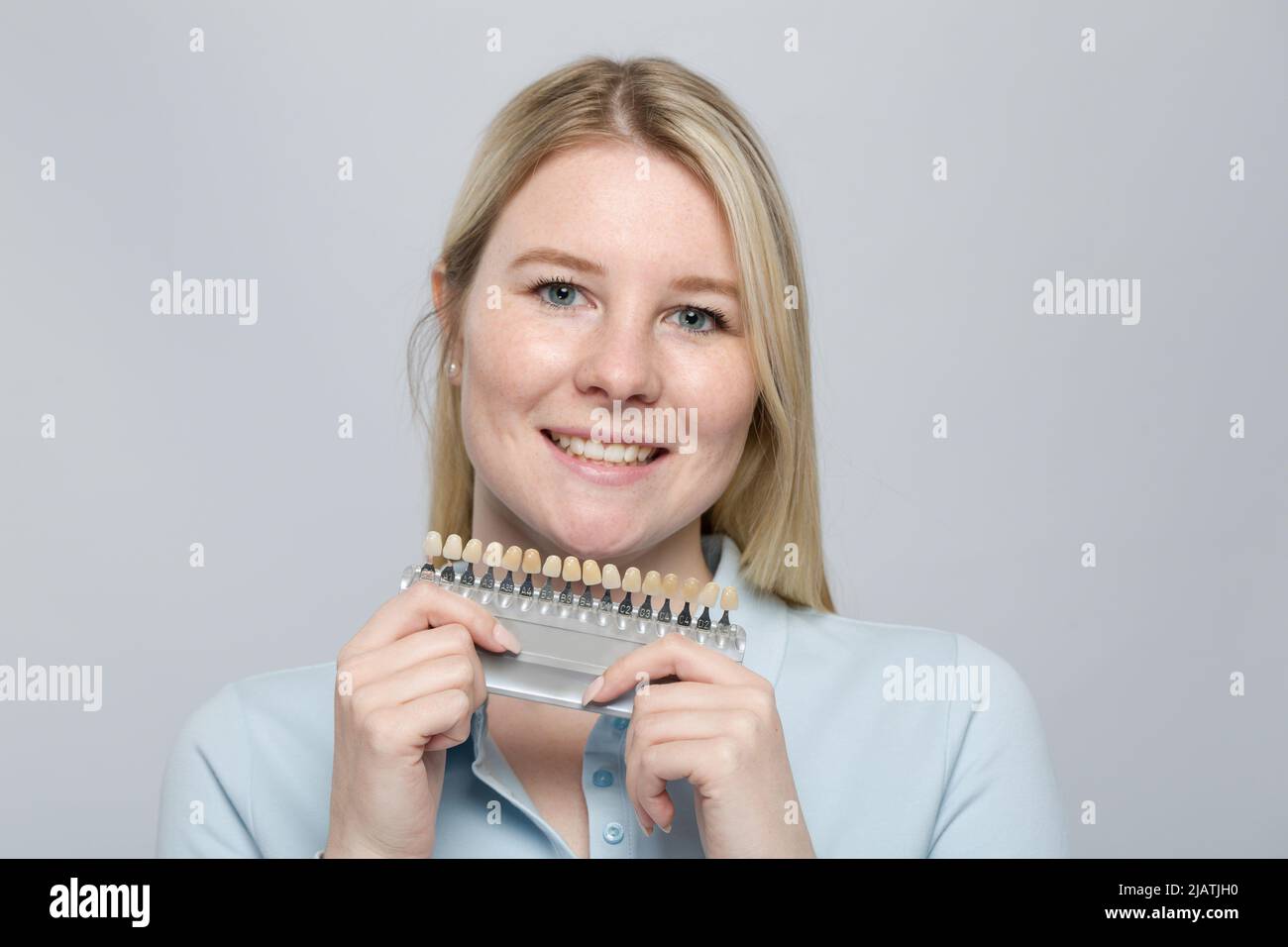 young woman presenting shade guide to check veneer of teeth for