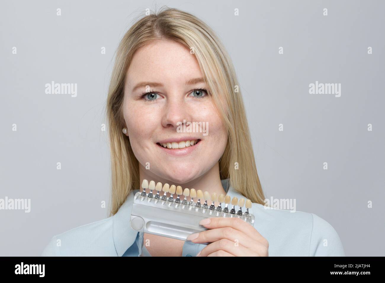 young woman presenting shade guide to check veneer of teeth for