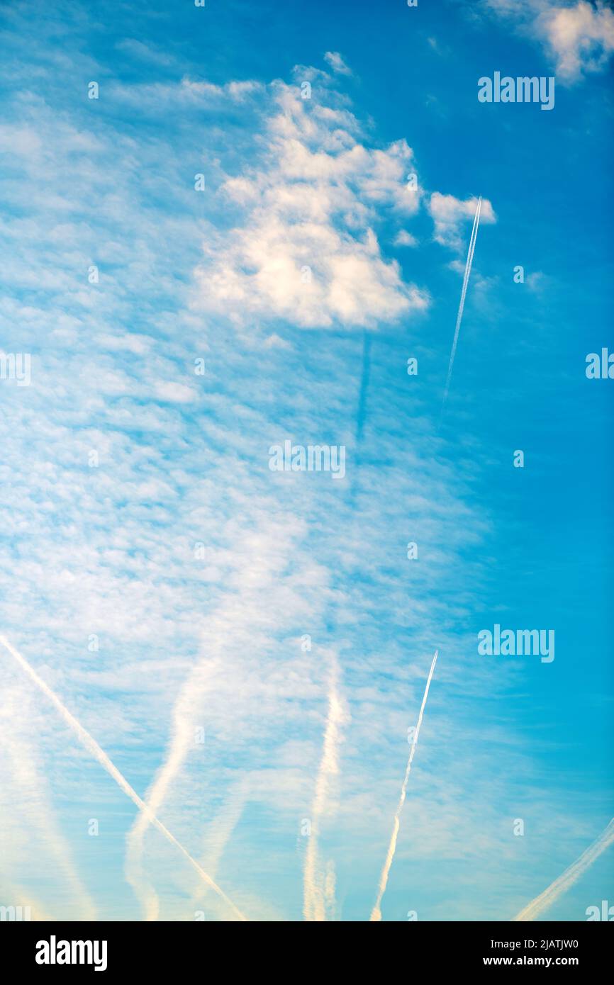 Airplane vapor trail or contrail pattern on blue sky with clouds from below Stock Photo