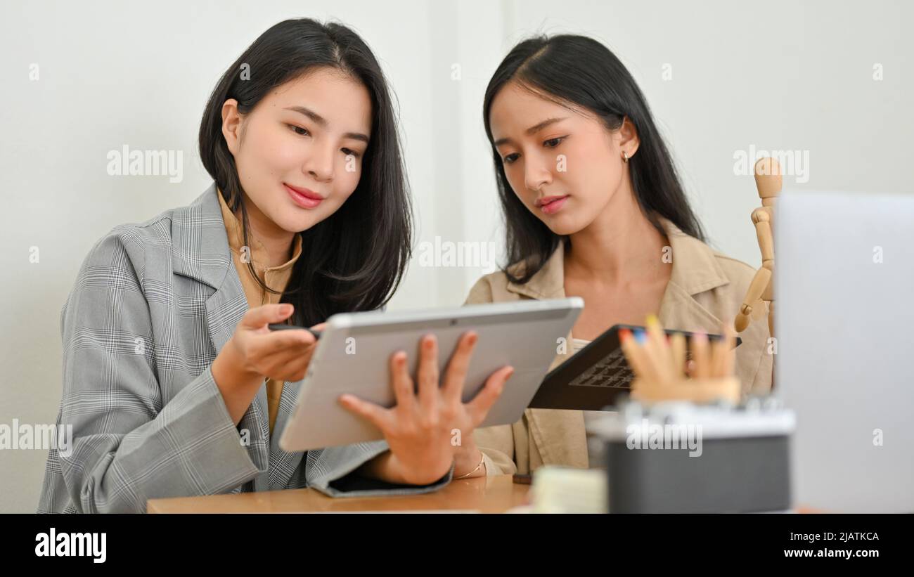 Professional asian businesswoman using digital tablet to teaching, training, and coaching a financial work to a new female worker in the office. Stock Photo