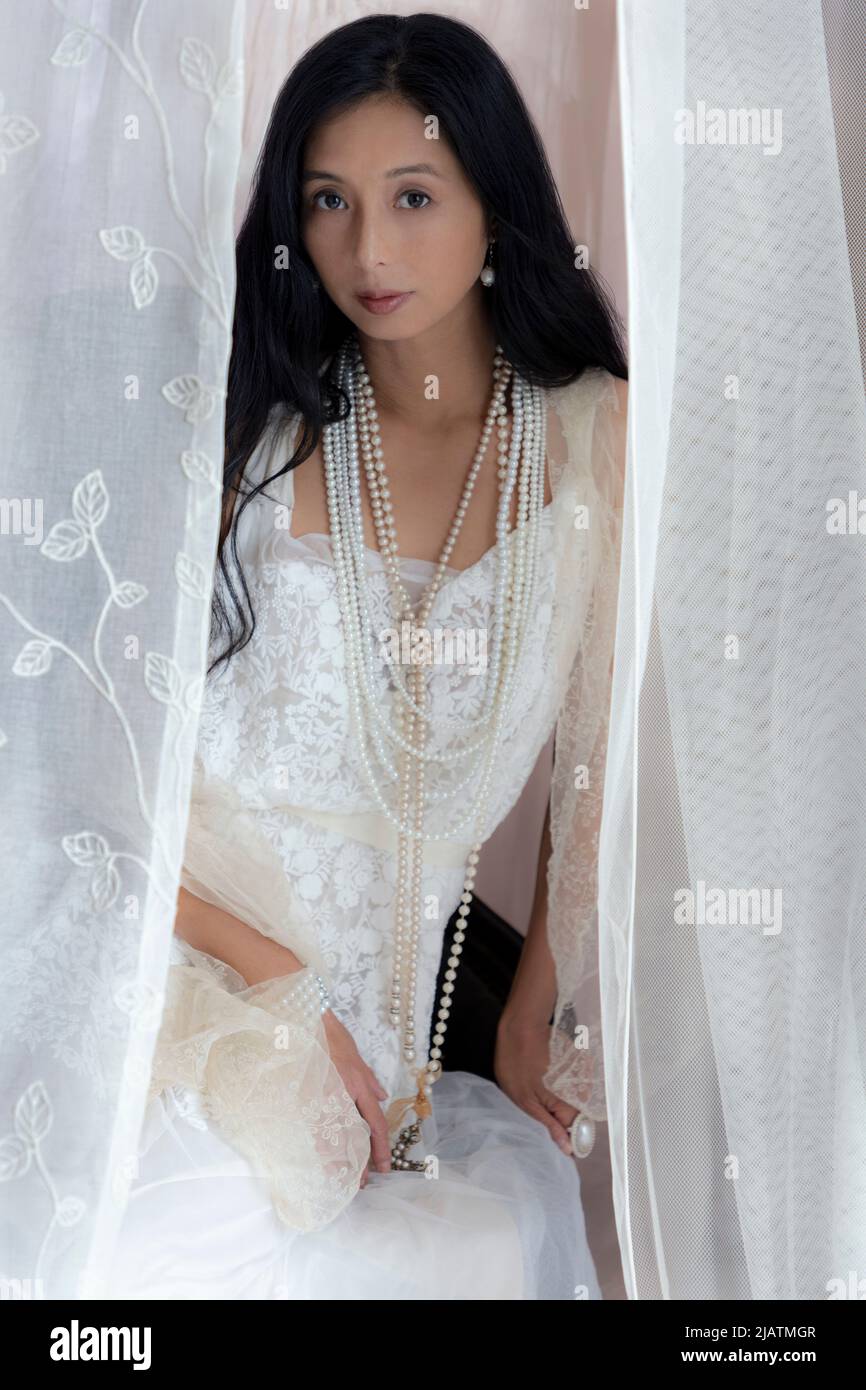 A beautiful Asian woman wearing a white lace dress and posing amongst  flowing sheer fabric Stock Photo - Alamy