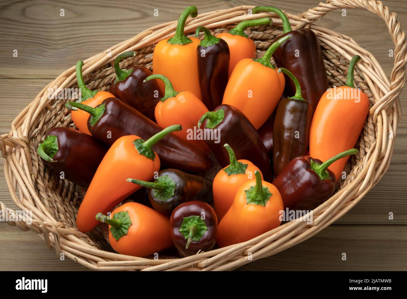 Basket with whole fresh orange and chocolate mini pointed bell peppers close up on wooden background Stock Photo