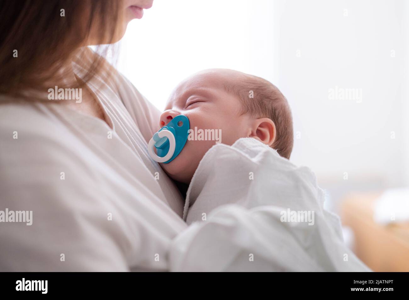 Little newborn baby boy sleeping with baby dummy on mother hands at