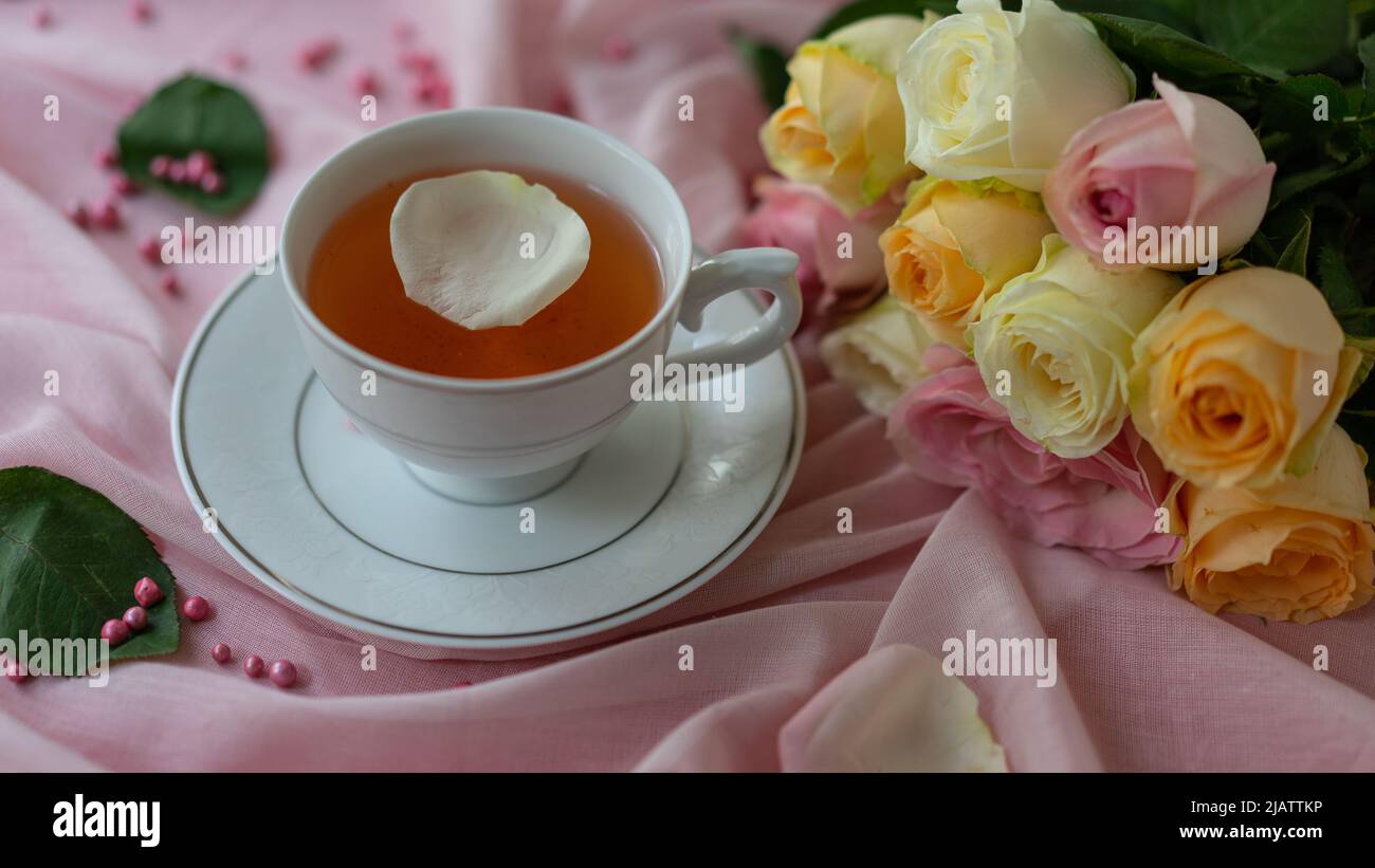 Eine Tasse Tee und ein Rosenstrauß auf rosa Hintergrund. Stock Photo