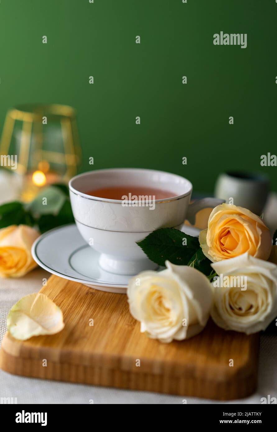 A cup of herbal tea and a bouquet of roses on a green background, Vertical Stock Photo
