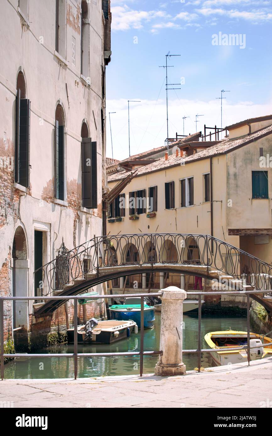 Romantic view on narrow street of Venice with old buildings and bridge above a canal. Boats float on the water, sunny day blue sky. Italian holidays. Stock Photo