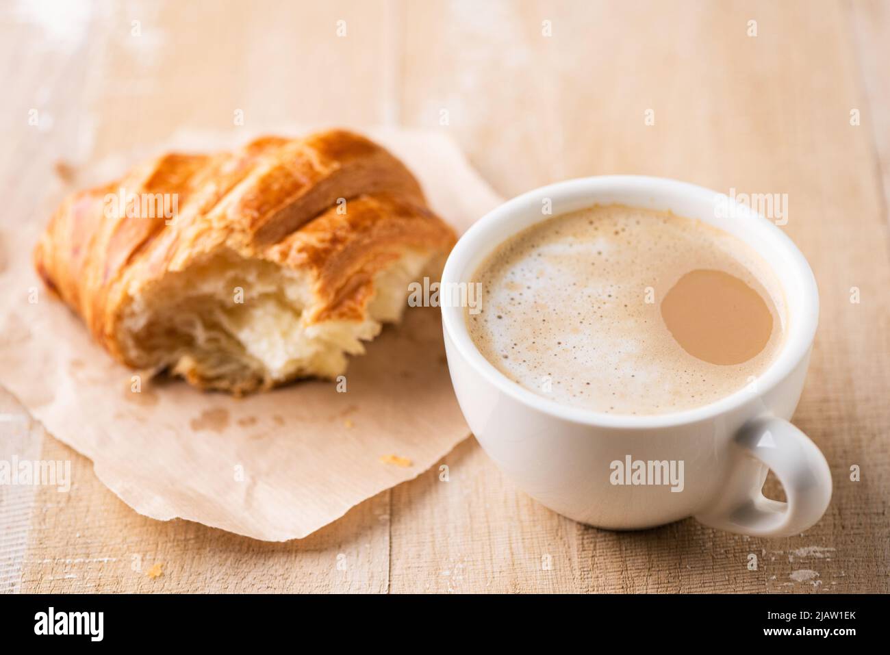 Cappuccino coffee and croissant on wooden table, croissant missing bite Stock Photo