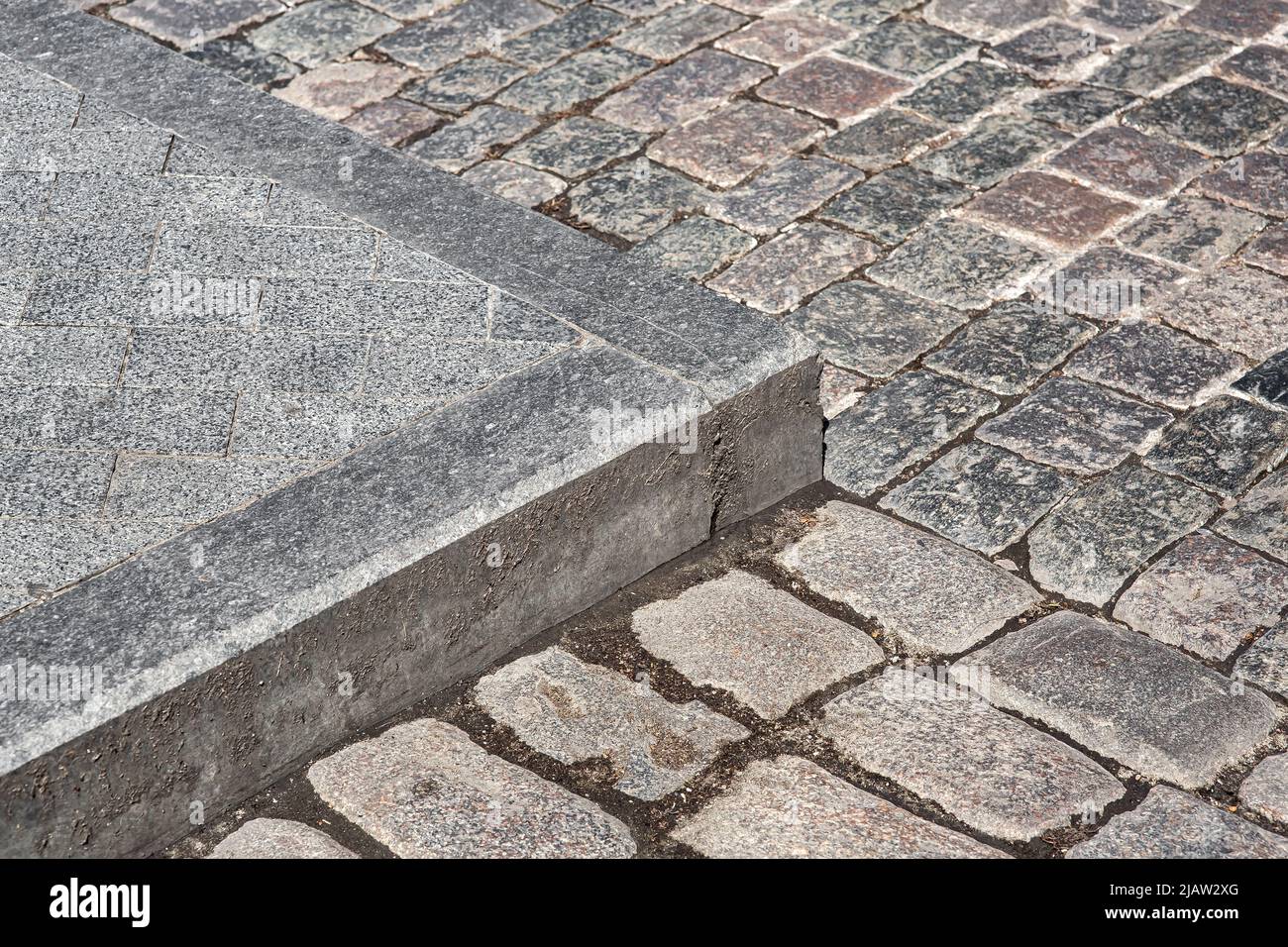 corner of a pedestrian sidewalk made of granite curb and stone rectangular brick tiles nearby a road paved with rough cut paving slabs close-up, nobod Stock Photo