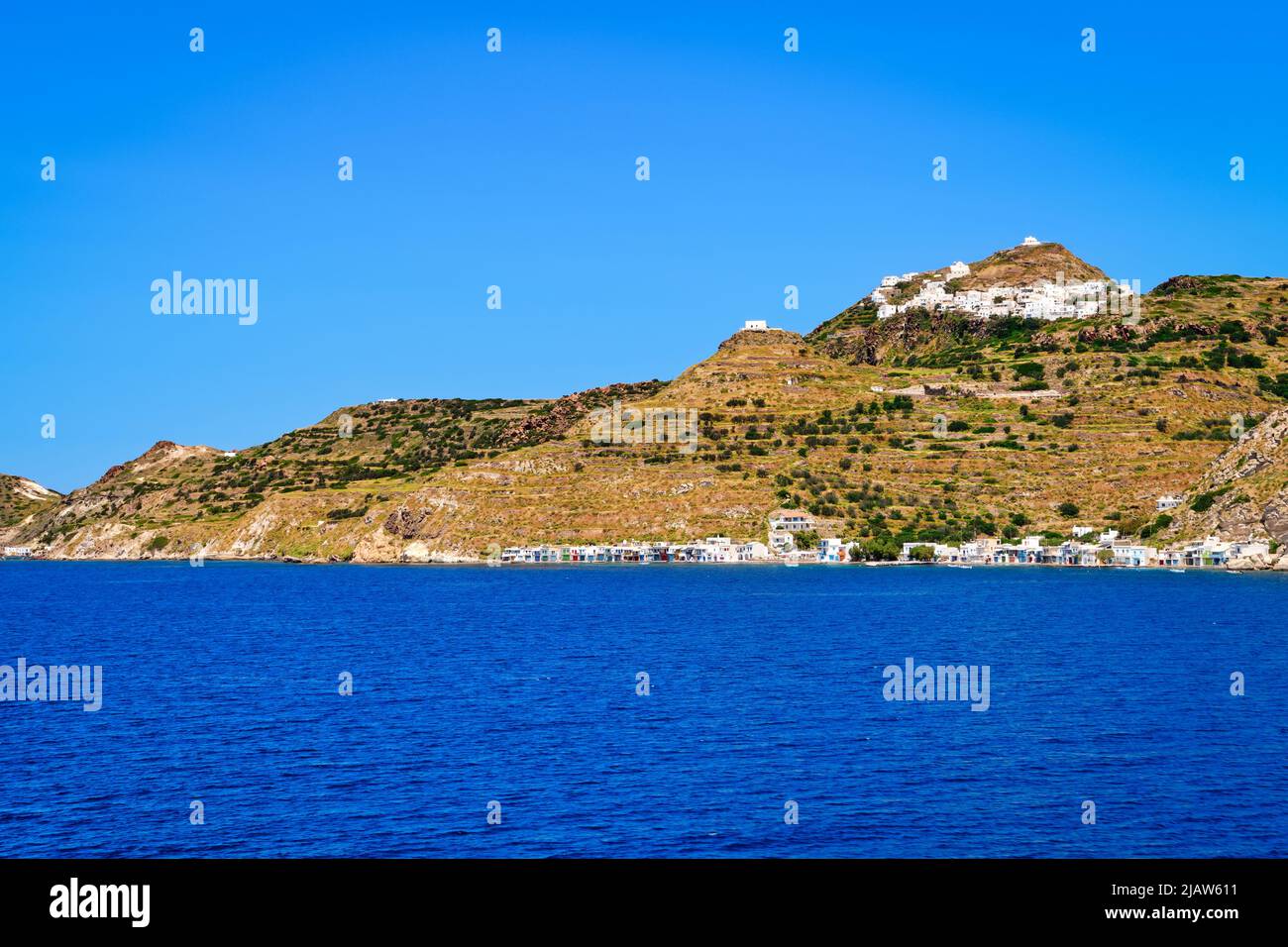 Beautiful summer day of Greek island town oh hill top by seafront. Whitewashed houses by waterfront. Mediterranean vacations. Milos, Cyclades, Greece. Stock Photo