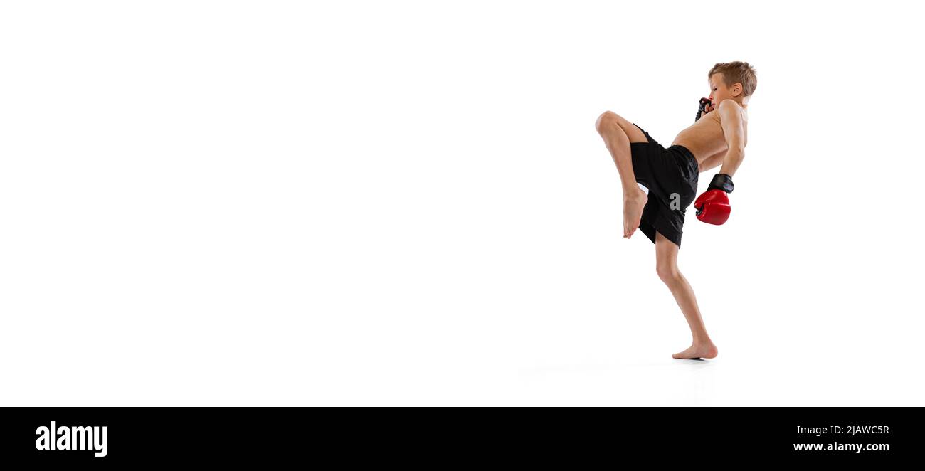 Little boy, kid in sports shots and gloves practicing thai boxing on white studio background. Sport, education, action, motion concept. Flyer Stock Photo