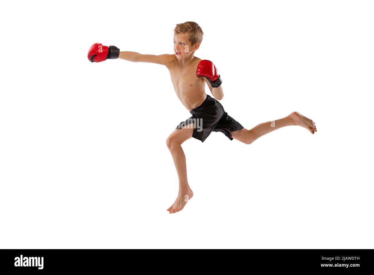 Punching. Little boy, kid in sports shots and gloves practicing thai boxing on white studio background. Sport, education, action, motion concept. Stock Photo