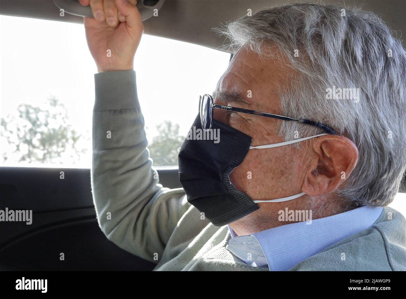 Older man sitting inside the car with lens and face mask Stock Photo