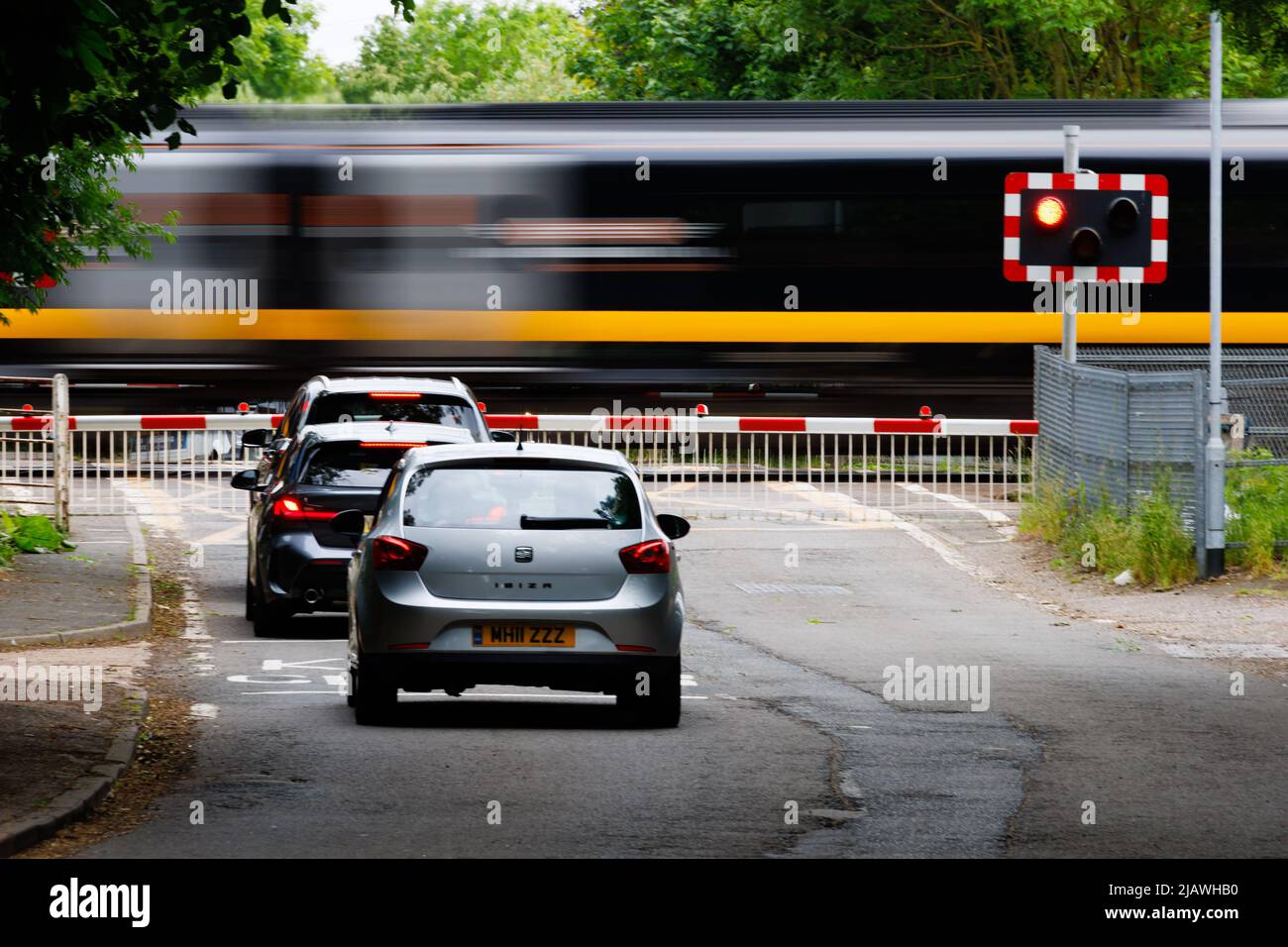 Cars waiting at the level crossing as a train speeds past on the East coast Mainline. Offord Cluny, Cambridgeshire, England Stock Photo