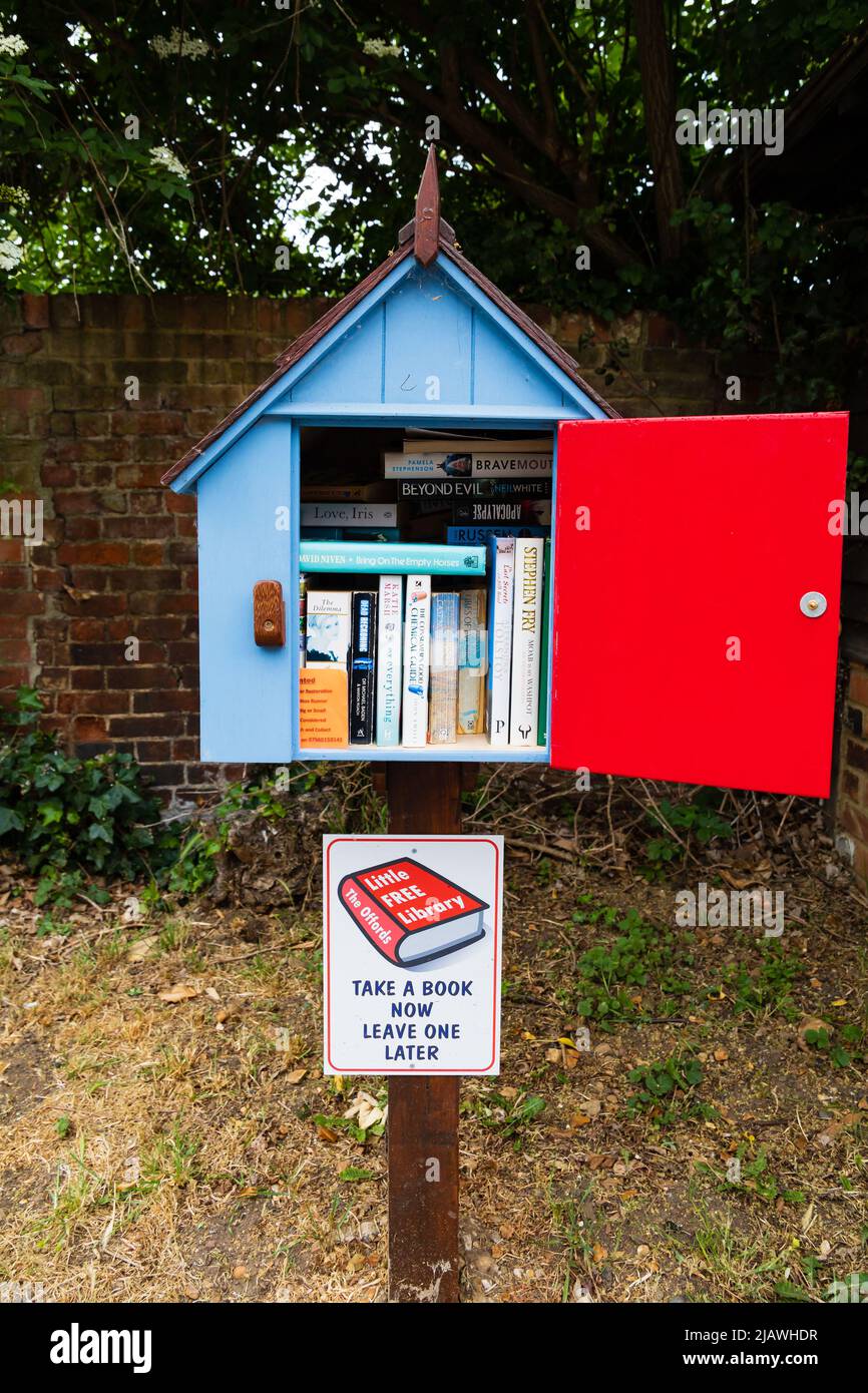 The Offords Little Free Library, book exchange box on post with door open showing a selection of books. Blue with red door. Offord Cluny, Cambridgeshi Stock Photo
