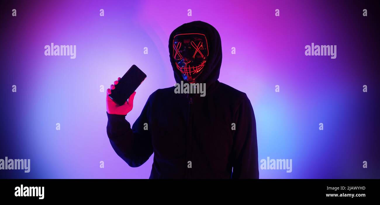 Anonymous hacker and face mask with smartphone in hand. Man in black ...