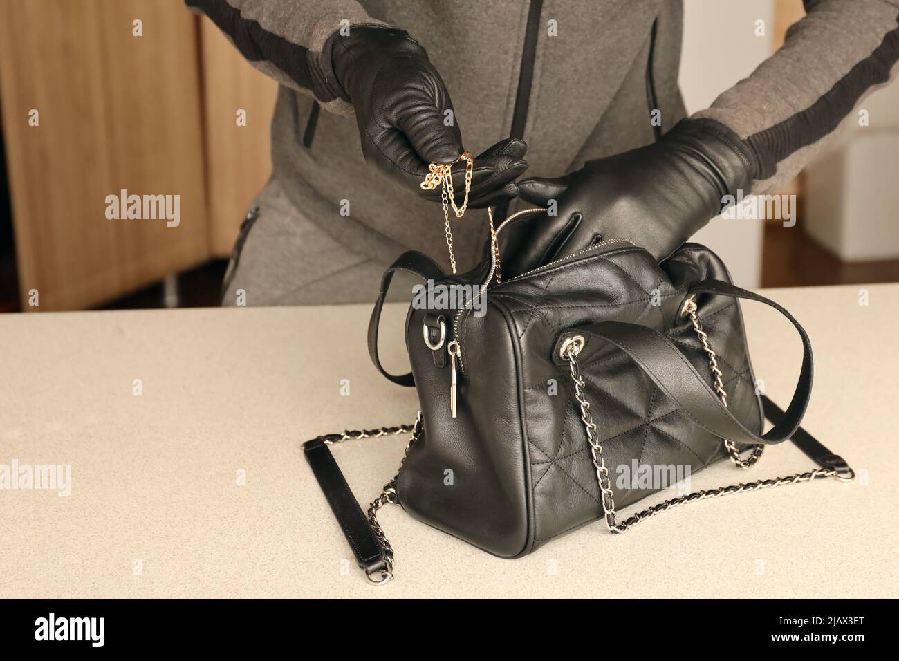 Robber in black outfit and gloves see in opened stolen women bag. The thief  takes out golden necklace from a womans handbag in kitchen interior Stock  Photo - Alamy
