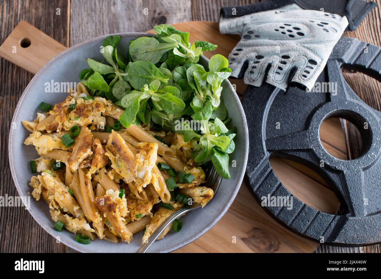 Fitness meal with pan fried whole wheat pasta and scrambled eggs. Served with a dumbbell on wooden table. Top view Stock Photo