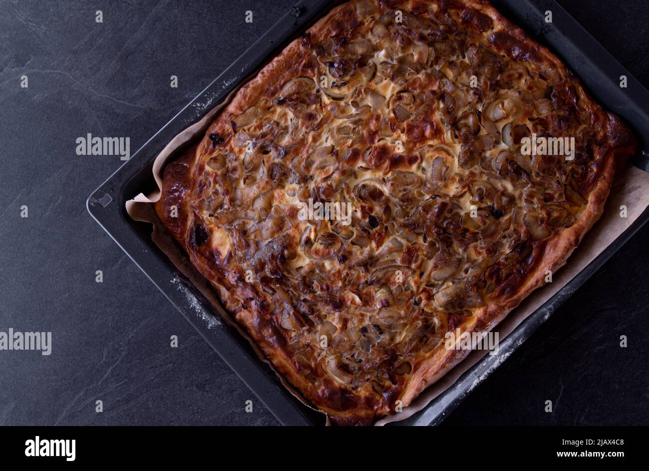 Onion cake on a baking tray isolated on dark table background with copy space. Top view Stock Photo